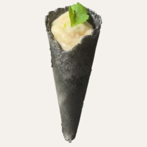 Cône noir texturé garni d'un houmous de haricot blanc onctueux et d'une petite feuille verte.