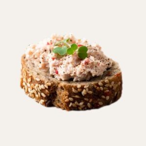 Gros plan sur "Le Croquant du Pêcheur" : une tartine au thon composée d'une terrine maison onctueuse sur une tranche de pain aux graines de sésame, décorée d'une herbe fraîche.