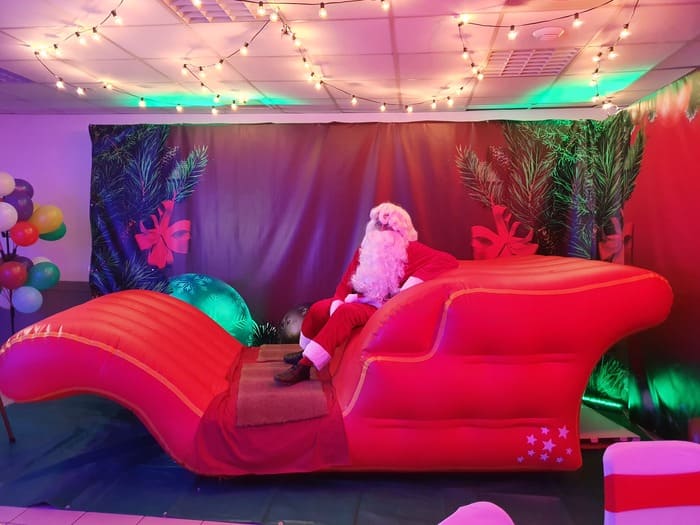 Traîneau Géant du Père Noël Gonflable a - Traiteur Événementiel Nantes & Vitré | Restonomade Le Père Noël assis dans le Traîneau Géant du Père Noël Gonflable, décoré pour un événement de fin d'année