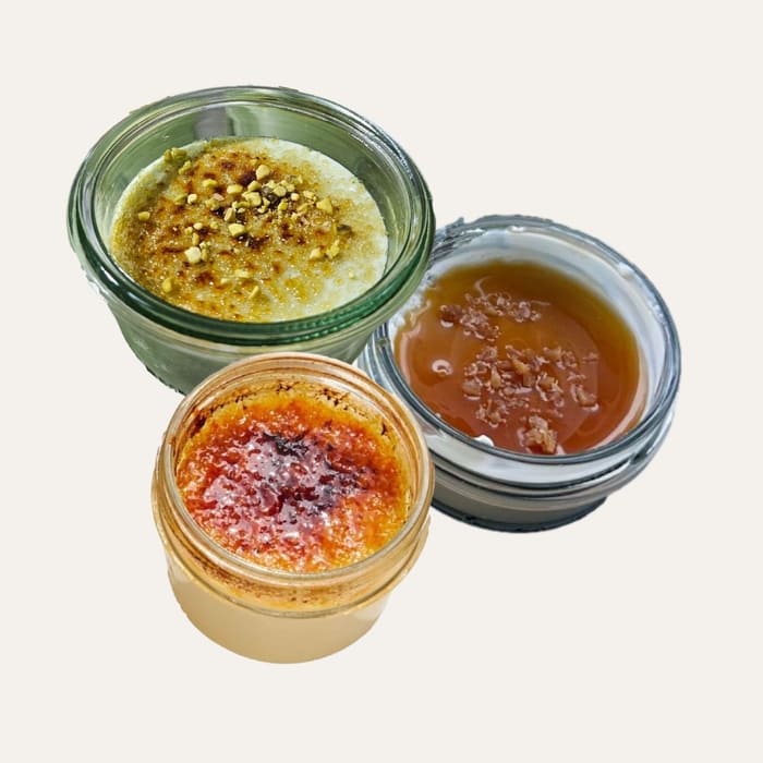 Trilogie gourmande - Traiteur Événementiel Nantes & Vitré | Restonomade Assortiment de trois verrines desserts en pot de verre : une crème brûlée pistache, une panna cotta caramel et une crème brûlée vanille.
