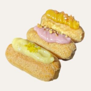 Assortiment de trois mini éclairs garnis : un à la fraise, un au citron et un au caramel.